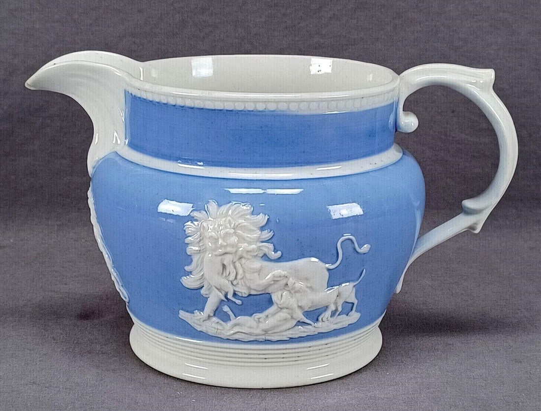 British Lions Snake Armorial Sprigged Jug C.1800: Antique British glazed porcelain jug with white sprig molded lion fighting dogs, lioness and snake, and an armorial crest under the spout over a blue ground. Unmarked. Circa 1800 to 1810.Has a glazed 