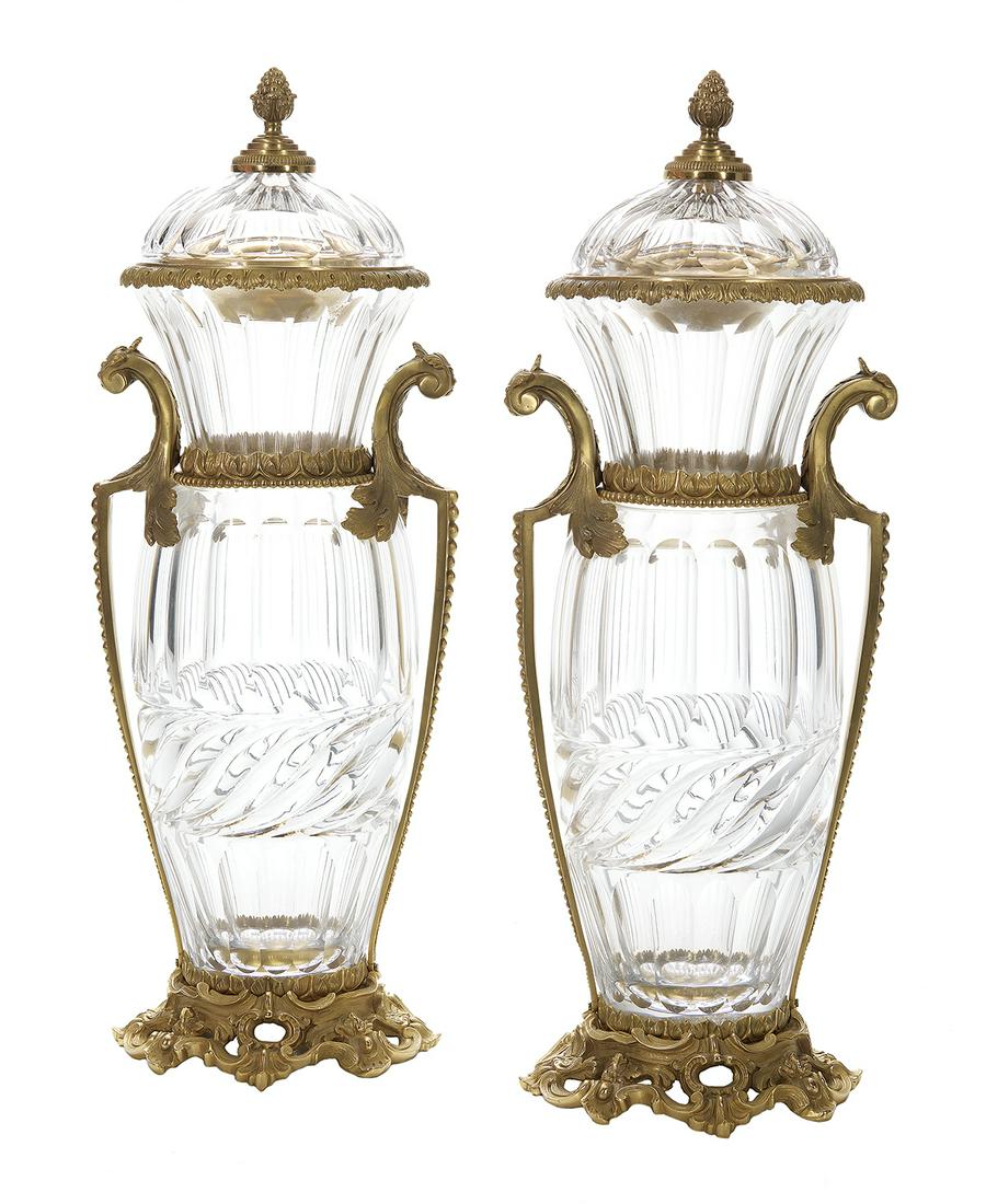 Pair of Gilt-Bronze-Mounted Cut Glass Urns: Pair of Gilt-Bronze-Mounted Cut Glass Garniture Urns first quarter 20th century, of rococo inspiration, the urns panel cut and gadrooned, and raised on pierced scroll-molded bases, the handles leaf-mo