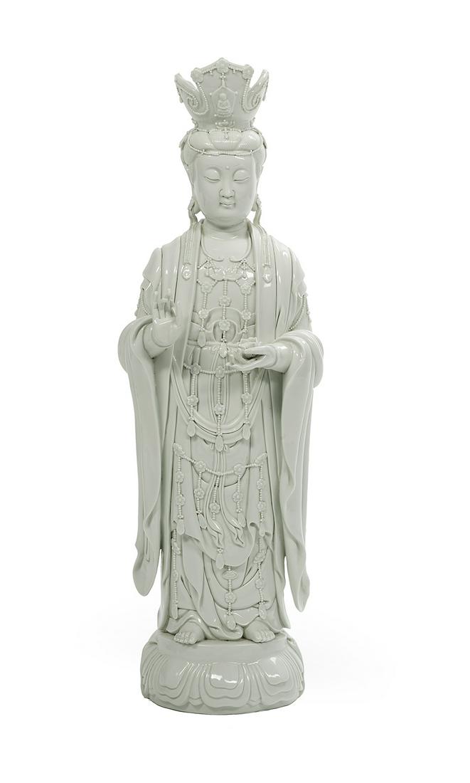 Blanc de Chine Figure of Guanyin: Blanc de Chine Figure of Guanyin 20th century, elegantly modeled standing on a lotus base, wearing traditional robes and headpiece, hand raised in abhaya mundra, with two impressed studio marks to the