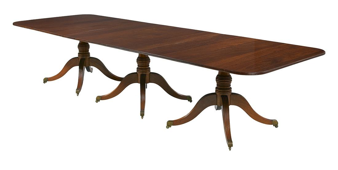 George III-Style Mahogany Dining Table: George III-Style Mahogany Dining Table the rounded rectangular top raised on three pedestals, each with a turned vasiform standard and four splayed and reeded legs ending in brass caps and casters, wi