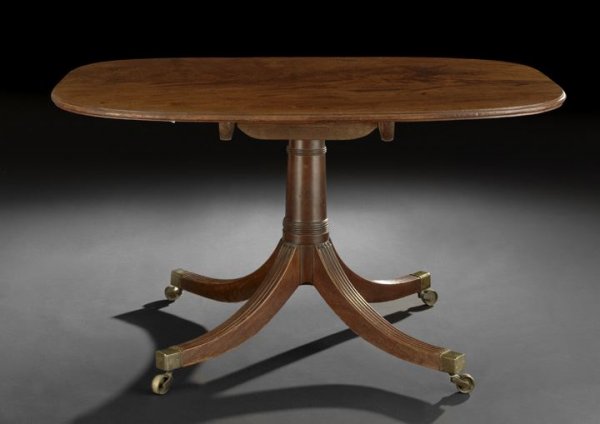 Regency Mahogany Breakfast Table: Regency Mahogany Breakfast Table, first quarter 19th century, the highly figured tilting rounded rectangular top raised on a turned columnar standard to four splayed and reeded legs ending in brass ca