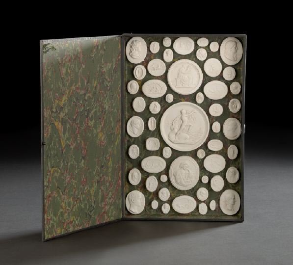 54 "Grand Tour" Plaster Casts of Intaglios: Collection of Fifty-Four "Grand Tour" Plaster Casts of Intaglios, the crisp plaster casts mounted against green-ground "bookbinder" paper within a leather-spined faux book , w. 14-1/2", d. 10".
