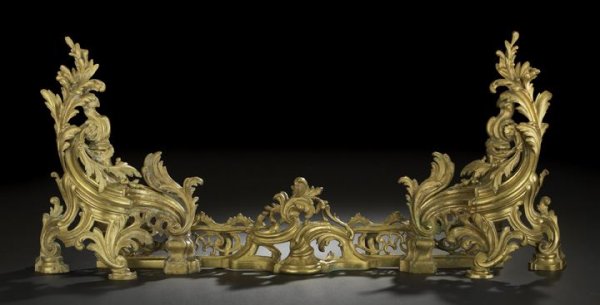 French Three-Piece Gilt-Brass Hearth Set: French Three-Piece Gilt-Brass Hearth Set, first quarter 20th century, comprised of a pair of chenets in the Louis XV style and a connecting reticulated brass fender centered with a foliate-scroll cart