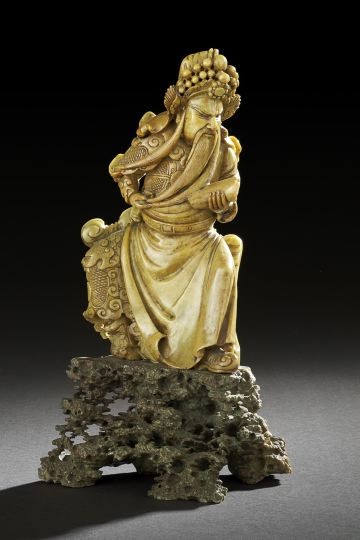 Chinese Carved Soapstone Figure of a Sage: Chinese Carved Soapstone Figure of a Sage, 20th century, the figure carved in caramel-colored stone and depicted in military dress holding a rolled scroll and pulling his beard, the figure attached to