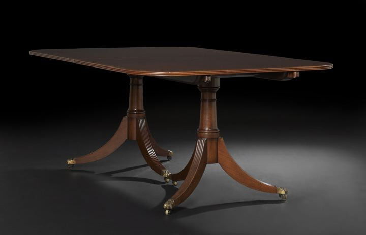 George III-Style Mahogany Dining Table: George III-Style Mahogany Dining Table, the rounded rectangular top banded and raised on two pedestals, each with a turned columnar standard to four splayed and reeded legs ending in brass paws on cas