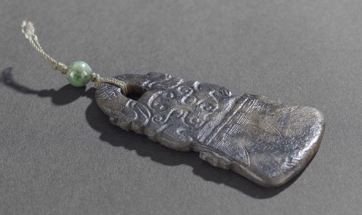 Rare Chinese Carved Jade Pendant,: Rare Chinese Carved Jade Pendant, possibly Zhou Dynasty (1050-221 BCE), the mottled black stone carved in low relief as an archaic axe, the blade engraved with stylized leaves, the top carved as a tao