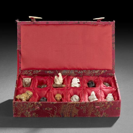 Twelve Japanese Netsuke and Small Carvings: Group of Twelve Japanese Netsuke and Small Carvings, of various materials including ivory, wood, bone and hardstone depicting birds, goats, snakes, masks, demons and skulls, brocade silk storage box, 