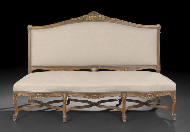 Louis XV-Style Fruitwood Settee,: Louis XV-Style Fruitwood Settee, early 20th century, the domed and padded back surmounted by a scrolling foliate shield crest with gilt accents, the padded seat above a foliate-and-shell-carved frieze