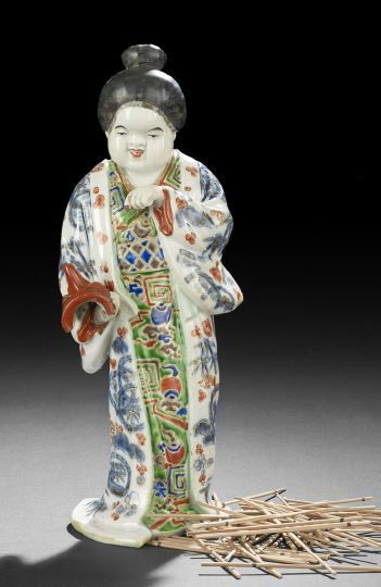 Japanese Polychromed Porcelain Figure of a Geisha: Japanese Polychromed Porcelain Figure of a Geisha, 20th century, the standing figure of a plump cheeked geisha clad in a flowing open robe over a kimono and holding a Noh mask of a long nosed demon, h
