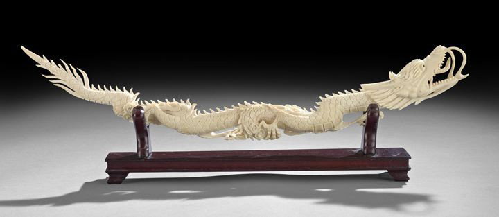 Chinese Carved Ivory Figure of a Dragon: Chinese Carved Ivory Figure of a Dragon, 20th century, carved horizontally from the tip of a tusk as a horned, scaly dragon with open-whiskered-mouth swallowing the Pearl of Wisdom, fitted wooden stan