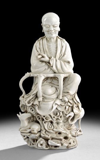 Chinese Blanc-de-Chine Figure of a Sage: Chinese Blanc-de-Chine Figure of a Sage, the bald headed figure clad in loose robes seated on a rockwork base with the figure of a deer, holding a scroll and seated before a cabriole-legged writing ta