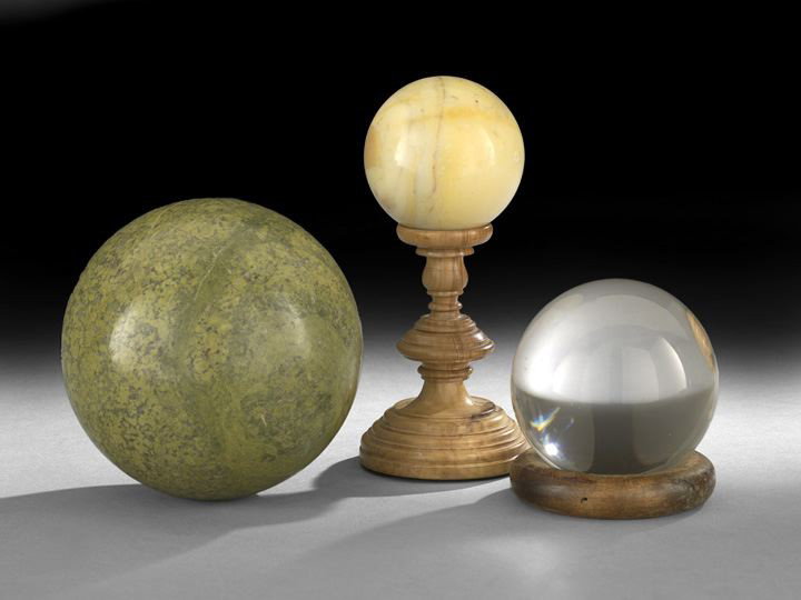 Three Decorative Spheres: Three Decorative Spheres, the largest of mottled green granite, dia. 5", the tan agate resting on a blond turned wood stand, h. 7-3/4", dia. 3-1/2" and the clear glass resting on a wooden ring, dia. 3