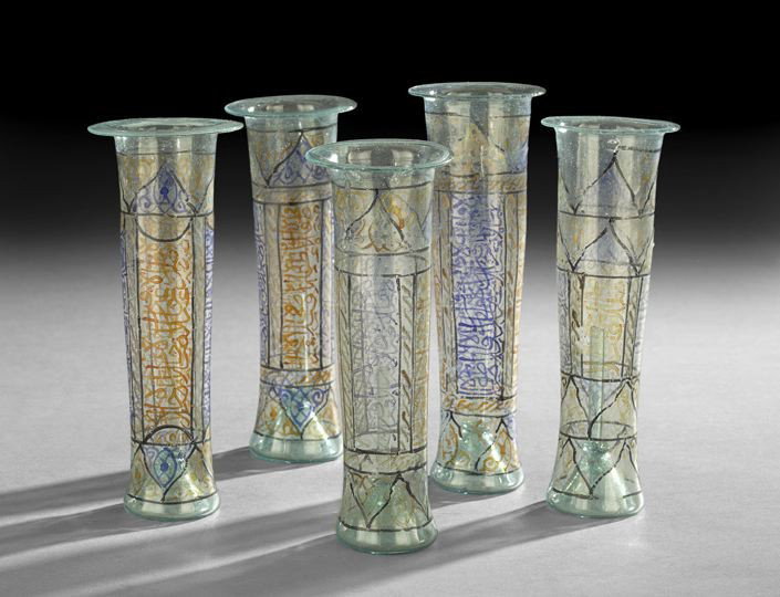 Five Middle Eastern Glass Vessels: Five Middle Eastern Glass Vessels, of pale green glass, the trumpet shaped vessels having lower tubes on the interior, decorated with a pattern of black Moorish arch windows and with Middle Eastern sc