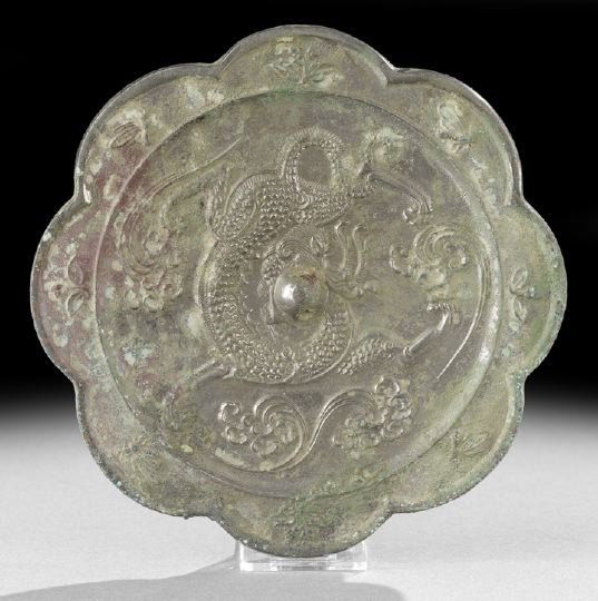 Chinese Cast-Silvered-Bronze Hand Mirror: Chinese Cast-Silvered-Bronze Hand Mirror, Ming Dynasty (1368-1644), of lobed outline cast on the face with a central boss with hole for silk cord, a central dragon among clouds and a border of flowers