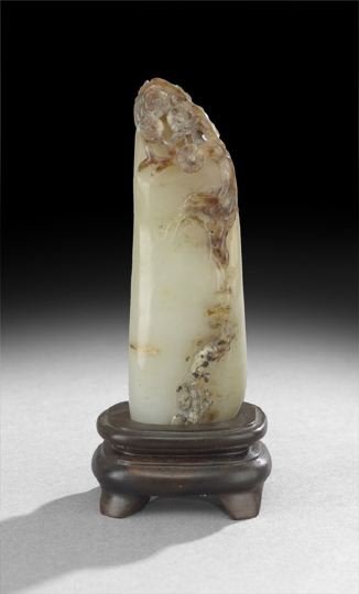 Chinese Carved Jade Elongated Mountain Carving: Chinese Carved Jade Elongated Mountain Carving, carved as one of the weird limestone southern mountains, the pale green stone with russet skin carved as flowering trees, presented on a wooden stand, h