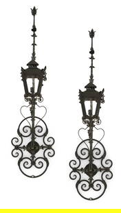 Pair of Large Black Metal Exterior Wall Lanterns: Pair of Large Black Metal Exterior Wall Lanterns20th century, in the Mediterranean taste, the pierced and scrolled backplates supporting the carriage lamps, beneath scrolled ornaments accented with fl
