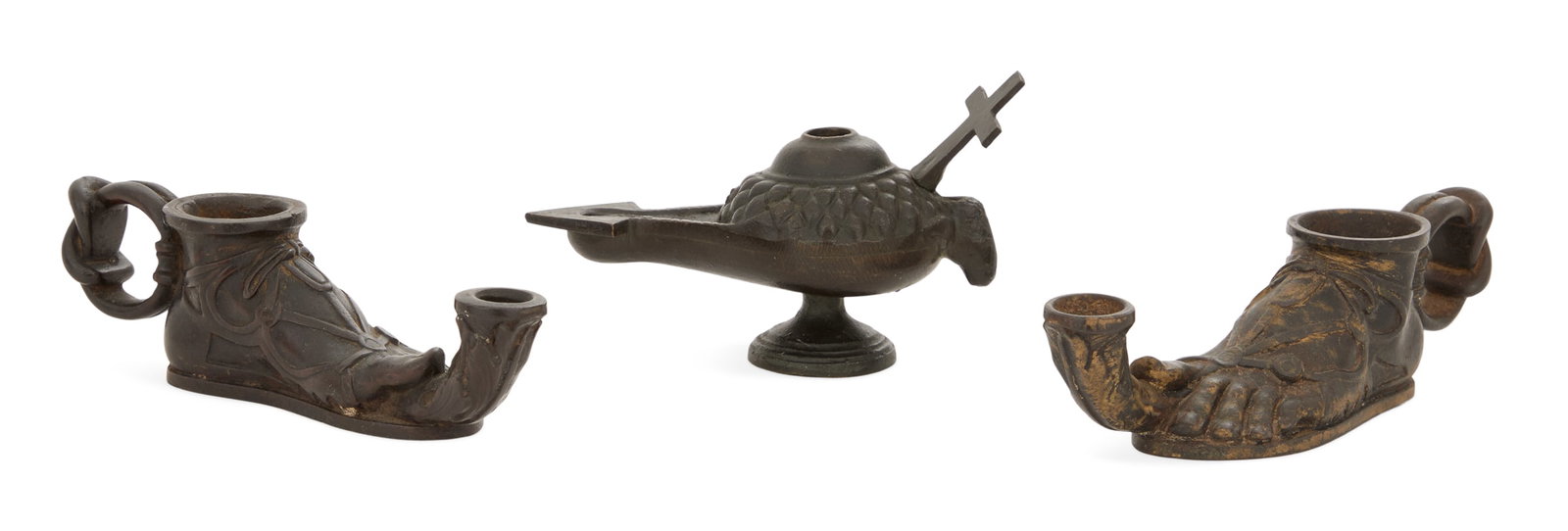 Three Patinated Bronze Grand Tour Oil Lamps: Three Patinated Bronze Grand Tour Oil Lamps 19th century, the collection including two lamps in the form of a sandal-clad foot, h. 2", w. 6-1/4", and a lamp with a cross and a ram's-head handle, h.