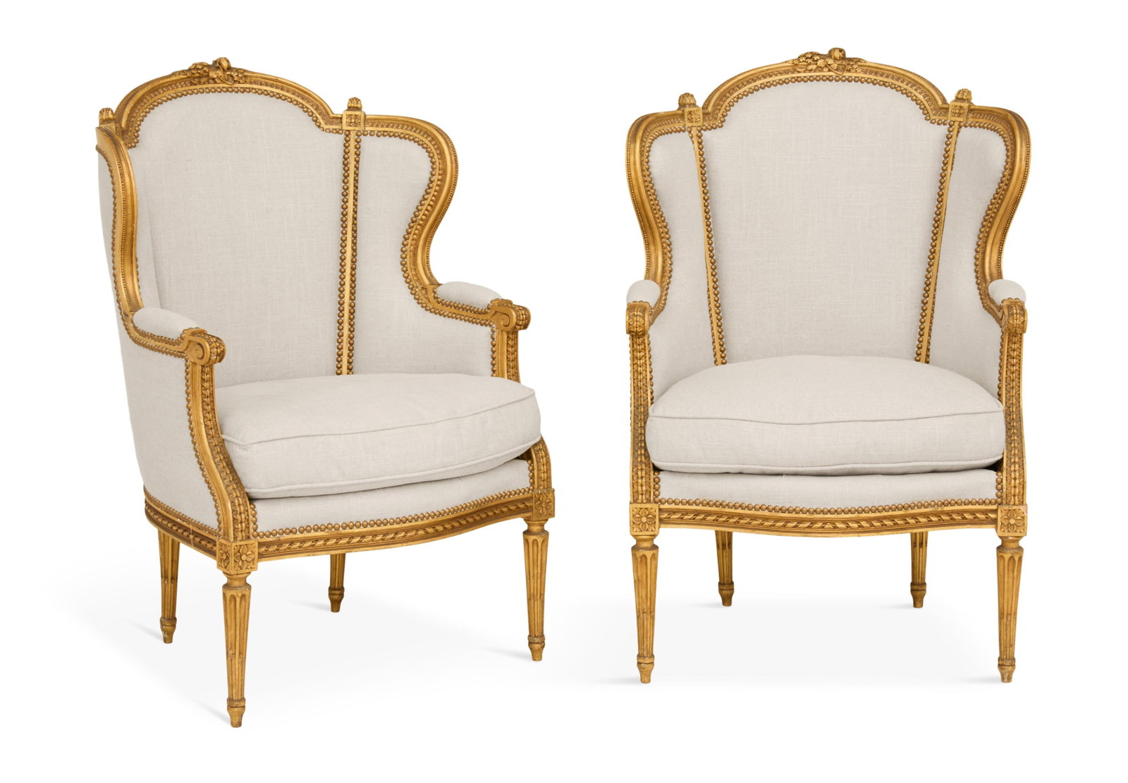 Pair of Louis XVI-Style Giltwood Wing Chairs: Pair of Louis XVI-Style Giltwood Wing Chairs early 20th century, the carved frames with a foliate-carved central crest, fitted with loose seat cushions and raised on turned and fluted legs ending in t