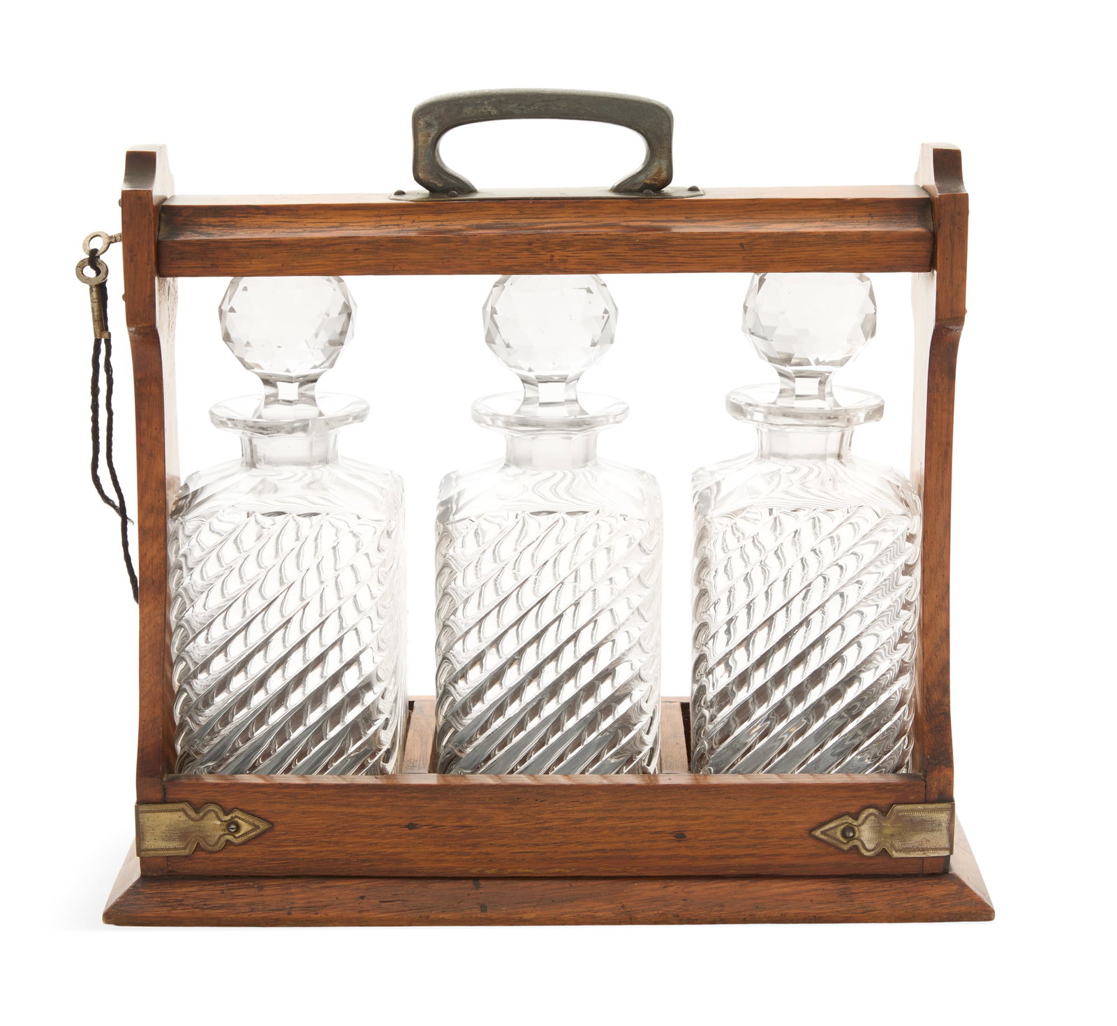 English Oak and Crystal Tantalus: English Oak and Crystal Tantalus ca. 1900, the Arts-and-Crafts-style carrier with brass-plated fittings and locking top, set with three molded and cut-crystal decanters decorated with angled reeding, 