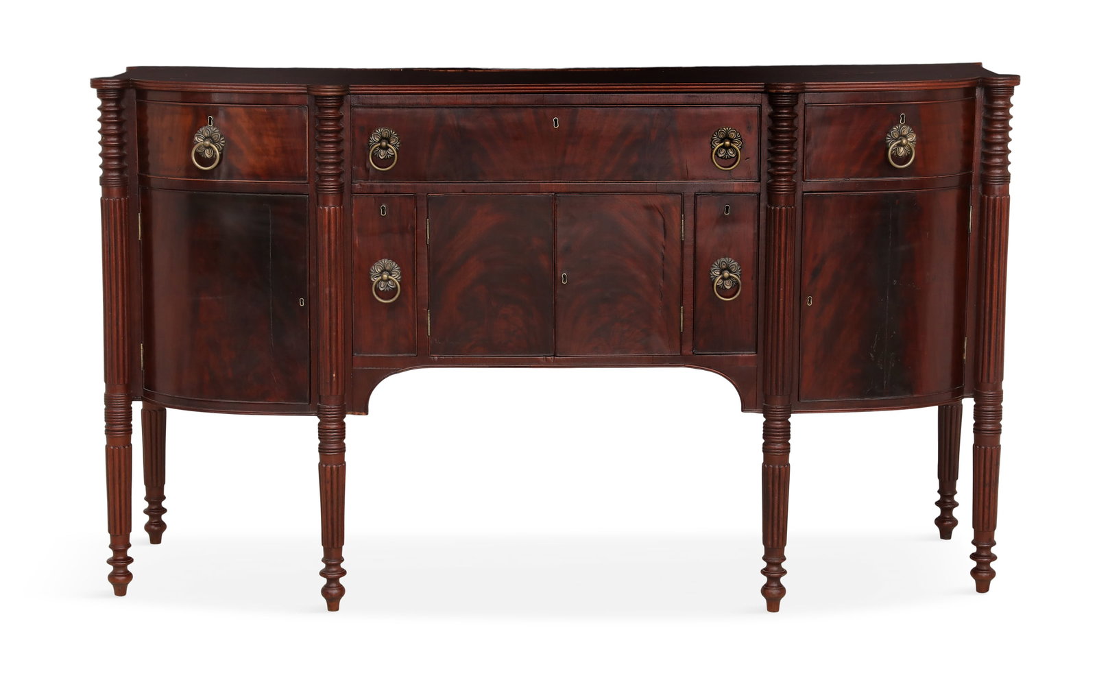 American Federal Mahogany Sideboard: American Federal Mahogany Sideboard early 19th century, the conforming shaped top with a reeded edge, over a row of three drawers, above a section of cabinets and bottle drawers, raised on reeded legs