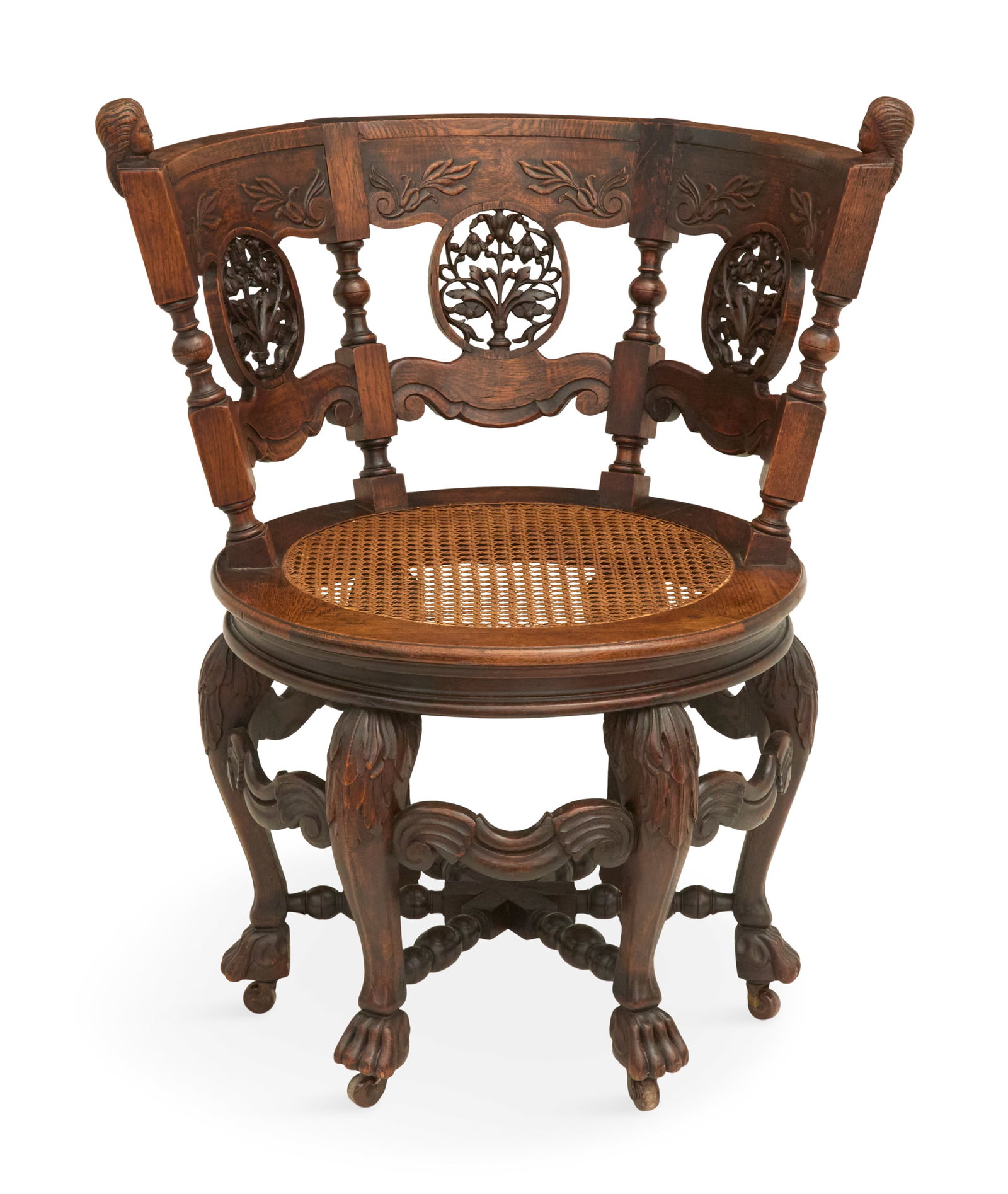 Continental Carved Oak Round-About Chair: Continental Carved Oak Round-About Chair ca. 1900, the curved back with circular pierced and carved foliate medallions, the arm posts with carved bust finials, with a caned seat and raised on carved