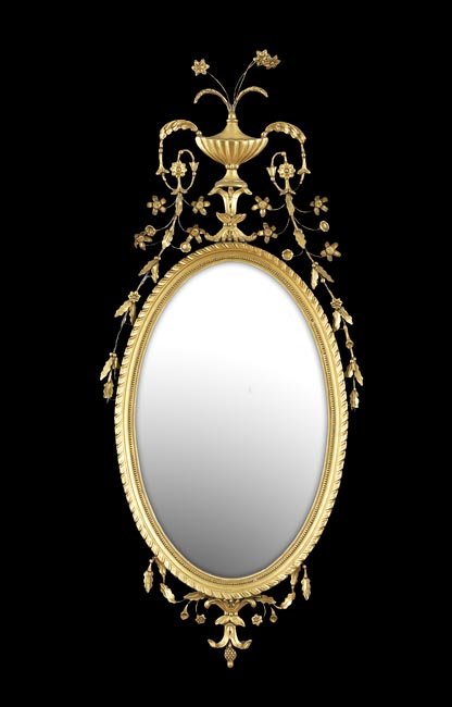 Edwardian Giltwood Mirror: Edwardian Giltwood Mirror, first quarter 20th century, in the Adam taste, the oval gadrooned frame decorated with an urn crest trailing sprays of flowers and scrollwork, h. 50", w. 21-1/2".