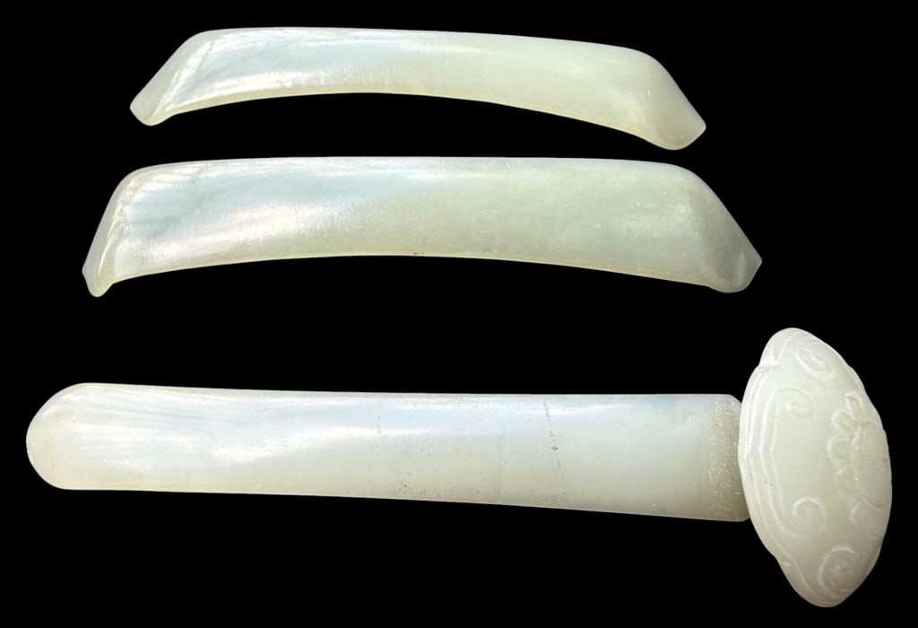 THREE CHINESE HAND-CARVED CELADON JADE HAIRPINS: Three Chinese hand-carved pale celadon jade hair ornaments comprising two elongated curved hairpins with tapered, angular ends and one larger pin in the form of a Ruyi scepter with a carved circular m