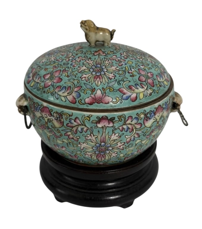 CHINESE PORCELIAN COVERED BOWL ON WOOD STAND: This Chinese polychrome enameled porcelain covered jar is presented on a tiered dark wood stand. The exterior is decorated with dense floral scrollwork and stylized lotus blossoms in a Famille Rose pa