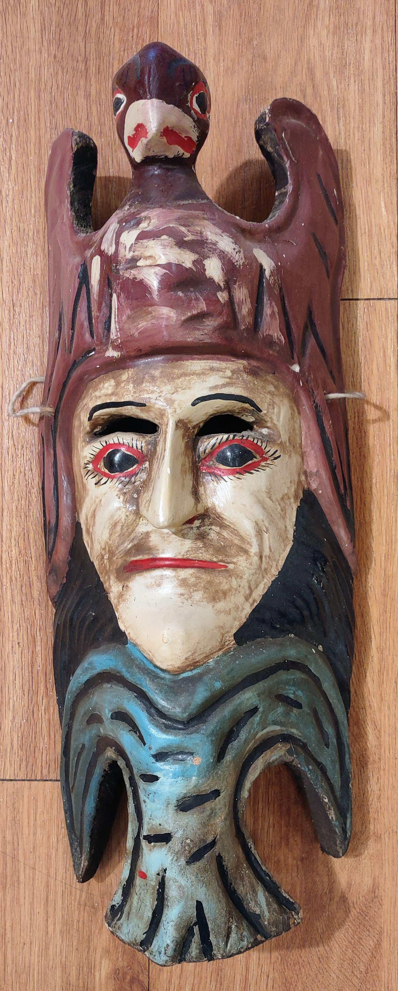Antique Mexican Mask: An antique distinctive hand-carved wooden Mexican mask featuring a stylized human face surmounted by a bird with outstretched wings forming part of the headdress. The mask is hand-painted in earthy