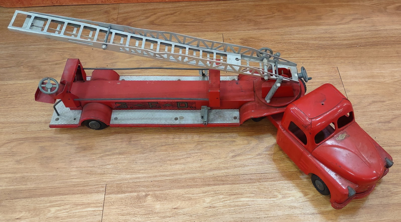 Structo Hydraulic S F D Hook & Ladder Truck 1950's: Vintage Structo Hydraulic S.F.D. hook and ladder truck, featuring pressed steel construction with classic fire department detailing. Equipped with extendable ladder and hydraulic-style mechanism chara