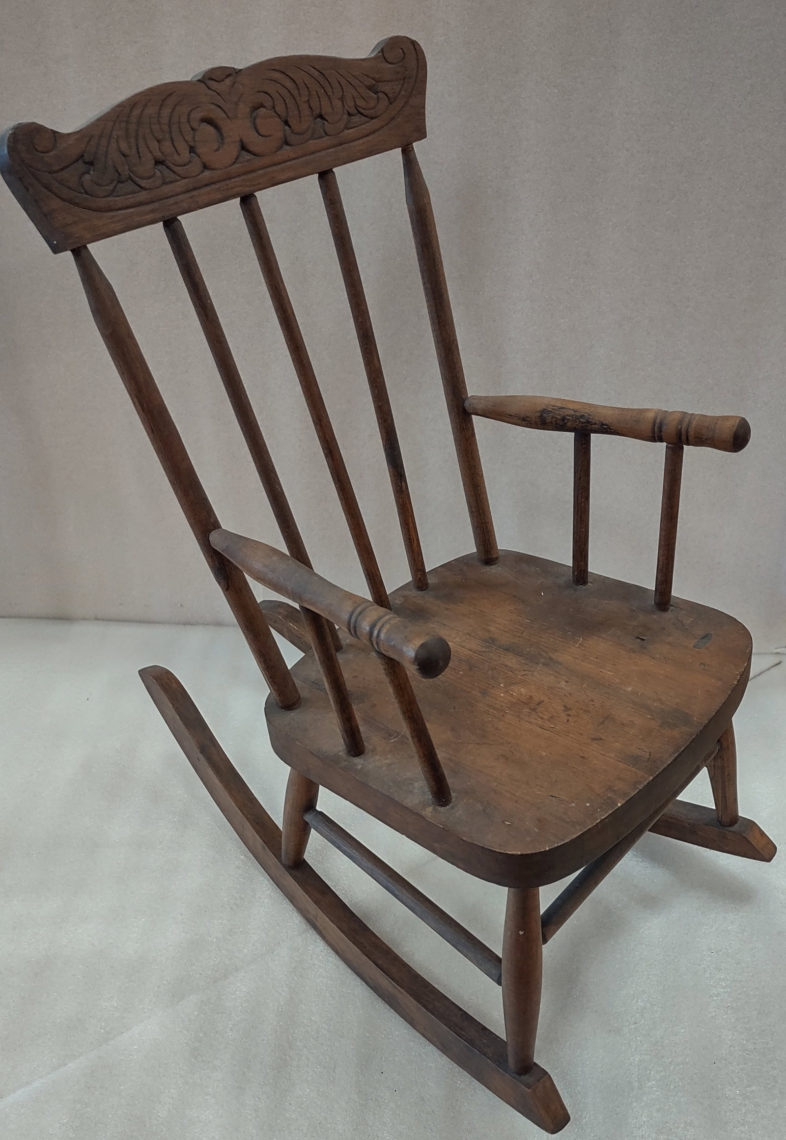 Antique Child's Rocking Chair: Antique child’s wooden rocking chair featuring a carved crest rail and spindle-back design with classic country charm. The diminutive armchair form reflects traditional craftsmanship and early