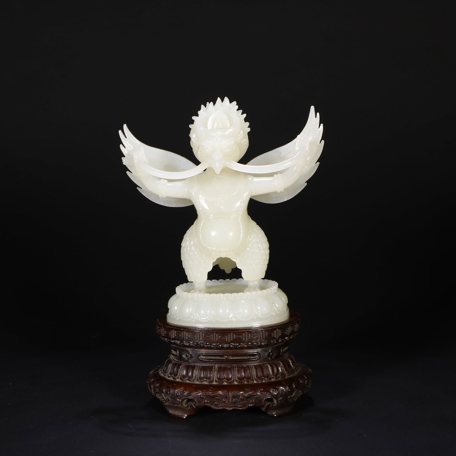 A Hetian jade carving of a Garuda: A jade statue of a mythical figure. Comes with a wooden base.H:10.6 cm W:10.1 cm