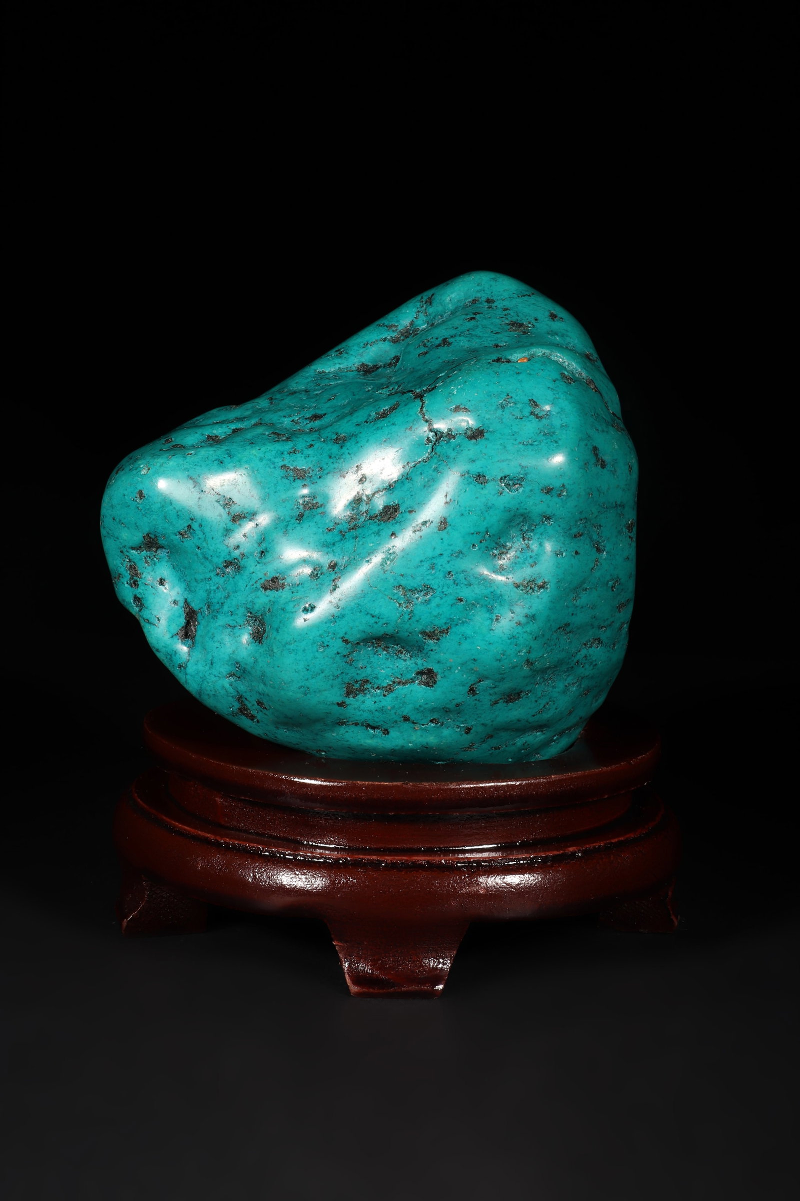 A Turquoise Ornament: A turquoise ornament with irregular shape and some black texture. Equipped with a detachable wooden base. Overall H: 14cm, Turquoise H: 12cm L: 11cm W: 10cm (Max)