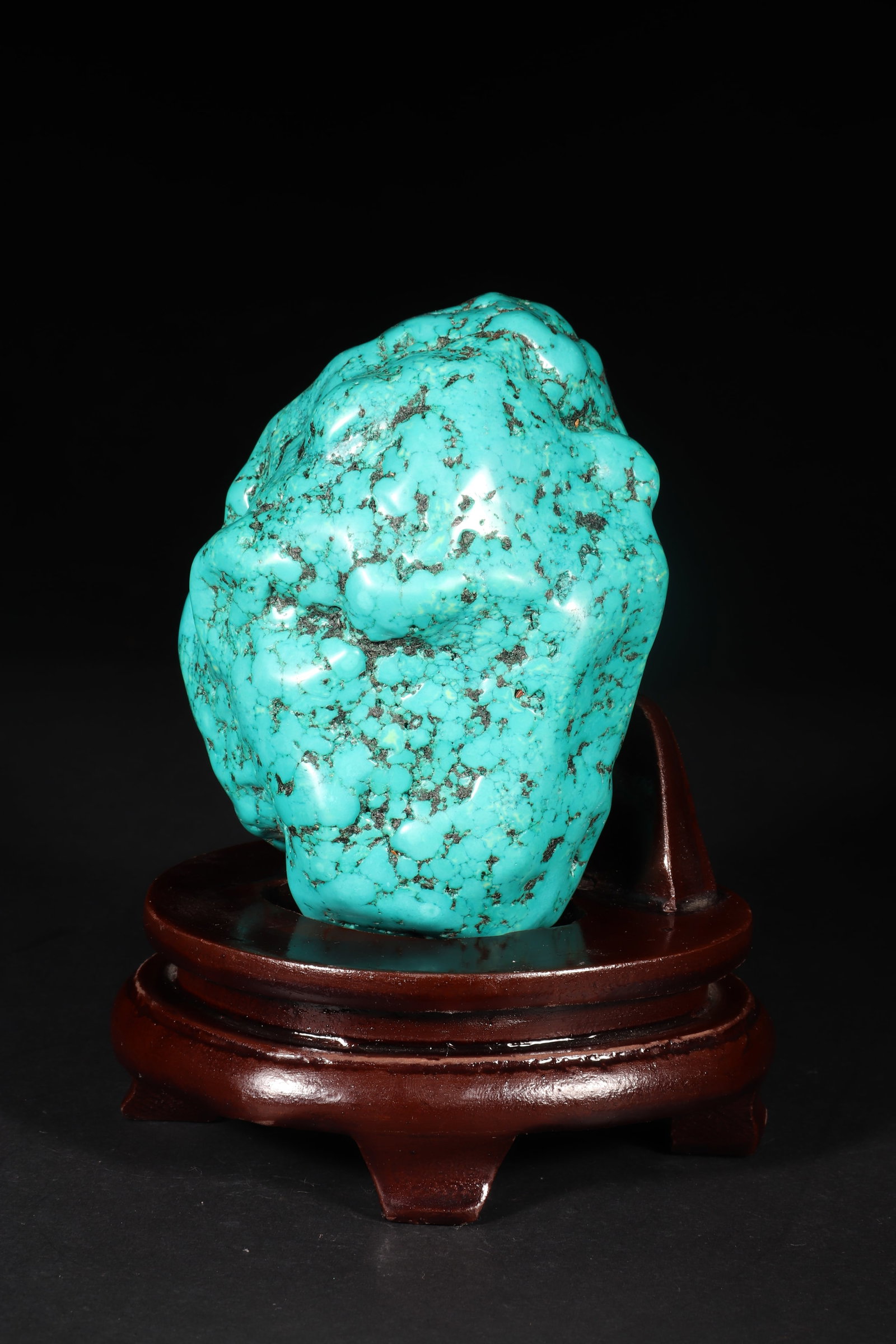 A Turquoise Ornament: A turquoise ornament with irregular shape and some black texture. Equipped with a detachable wooden base. Overall H: 14.5cm, Turquoise H: 11cm L: 9.5cm W: 7.5cm (Max)