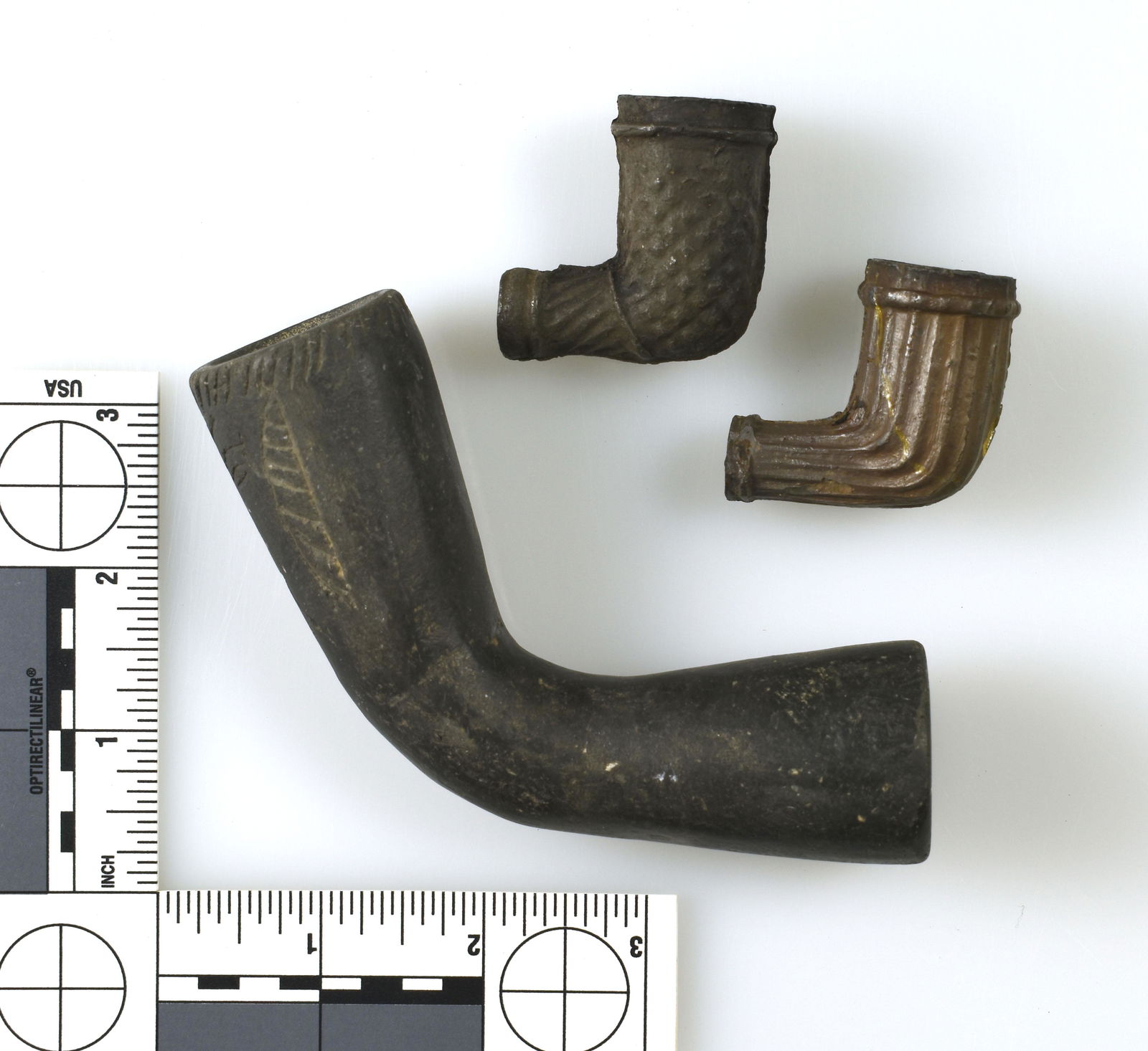 Three Indian Pipe Forms: Two trade era examples. And one 5" fired clay elbow with incised human face and other designs. Largest is decorative and smaller ones are of the trade period. All three in excellent condition.