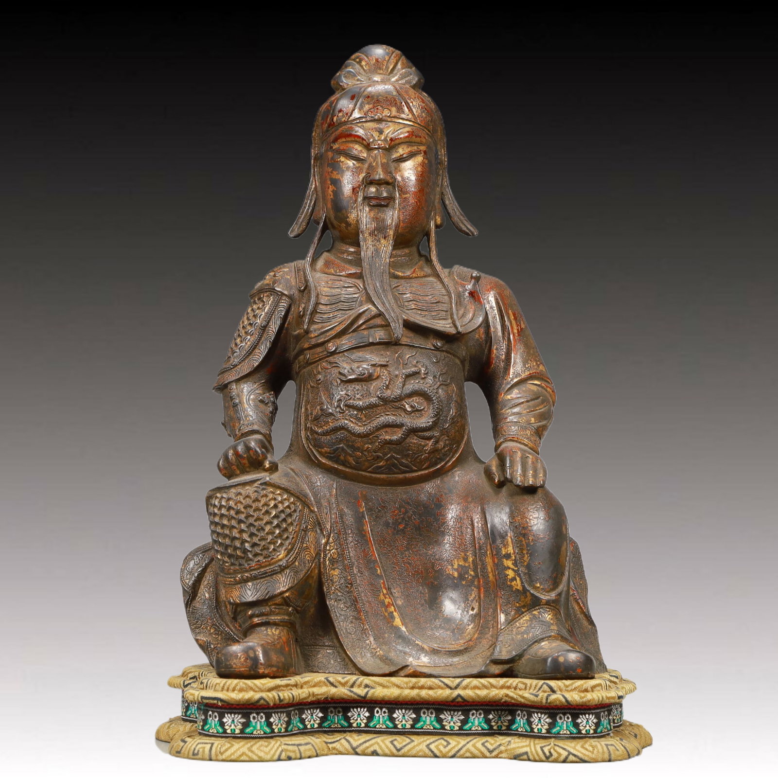 A Precious Gilt-Bronze Figure Of Guan Gong: A Precious Gilt-Bronze Figure Of Guan Gong. The bearded figure is seated with a meditative expression,body rendered clad in an armor,the belly area cast in detail with a sinuous,scaly dragon. Chinese 
