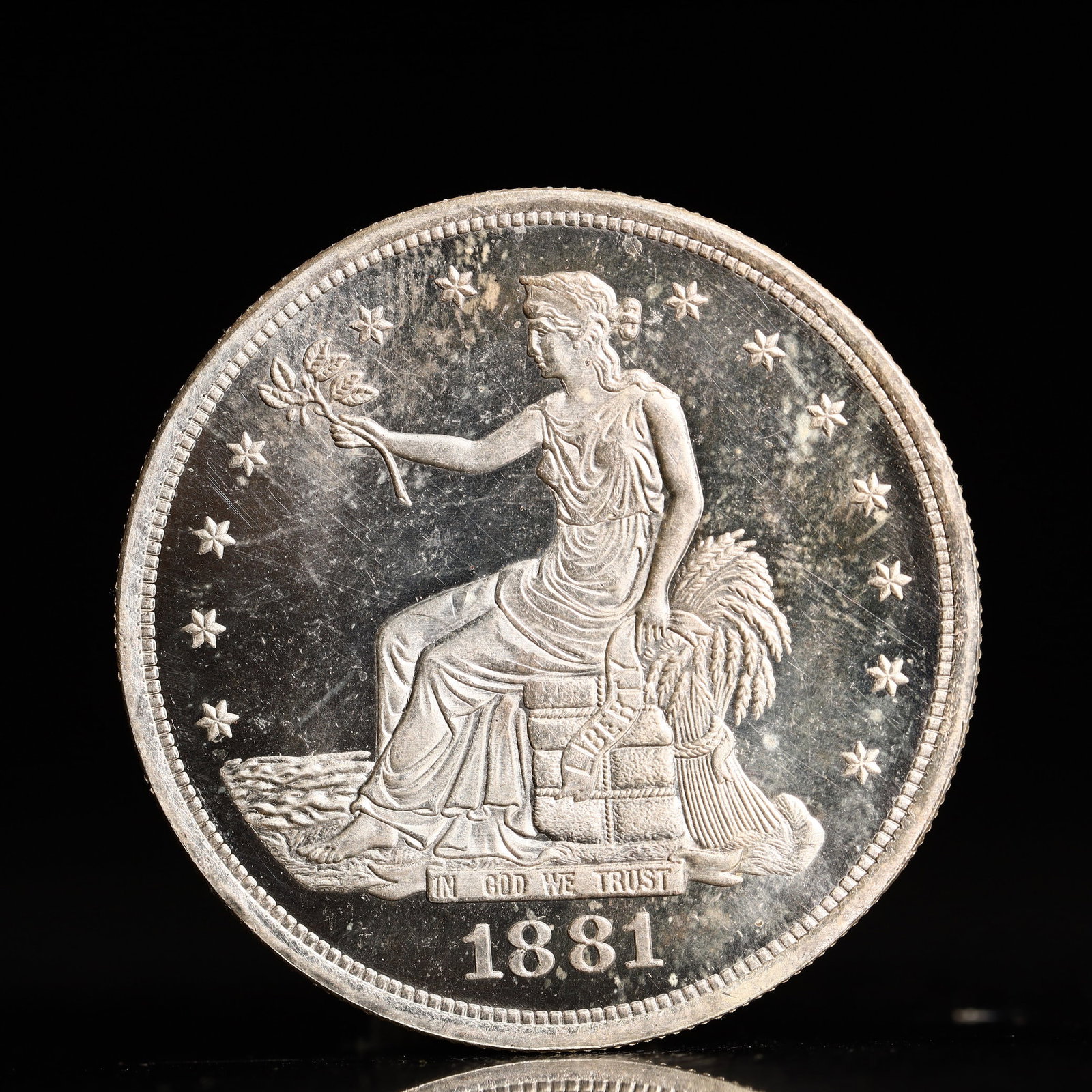 USA Trade Dollar 1881 Coin: American coin. Obverse: Liberty seated on a pedestal facing the sea to the left holding olive branches surrounded by 13 stars. IN GOD WE TRUST / LIBERTY / 1881. Reverse: An eagle holding branches with