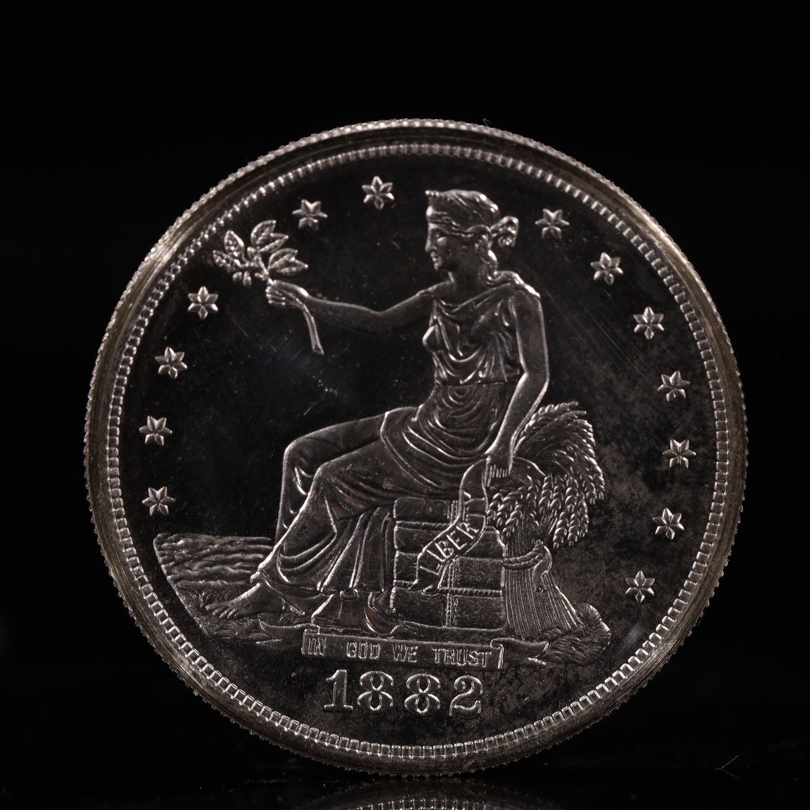 USA Trade Dollar 1882 Coin: American coin. Obverse: Liberty seated on a pedestal facing the sea to the left holding olive branches surrounded by 13 stars. IN GOD WE TRUST / LIBERTY / 1882. Reverse: An eagle holding branches