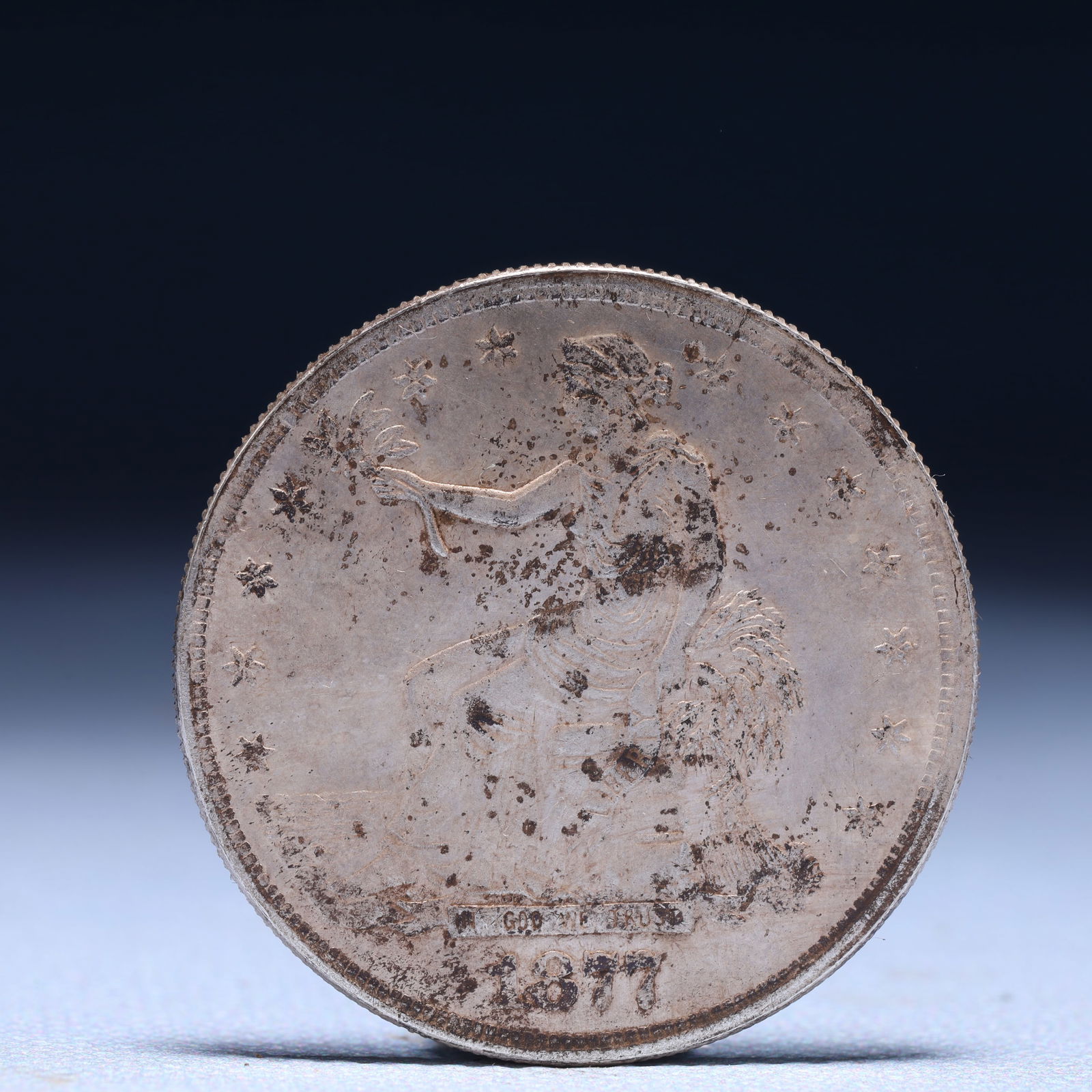 USA Trade Dollar 1877 Coin: American coin. Obverse: Liberty seated on a pedestal facing the sea to the left holding olive branches surrounded by 13 stars. IN GOD WE TRUST / LIBERTY / 1877. Reverse: An eagle holding branches