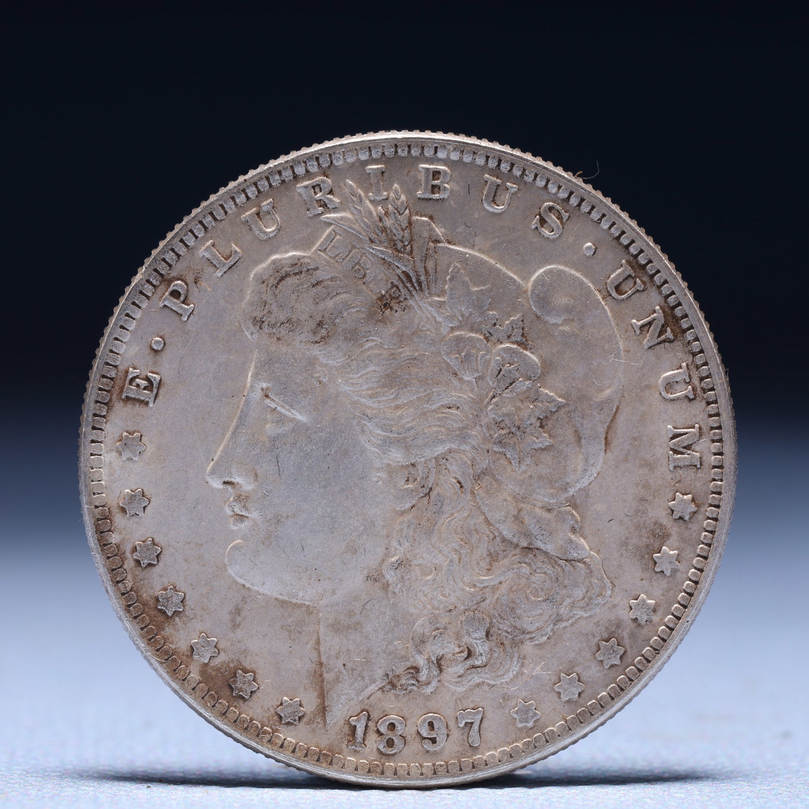USA Morgan Dollar 1897 Coin: Obv: profile bust with date below and E PLURIBUS UNUM legend and stars around. Rev: eagle with In God we trust above within wreath with UNITED STATES OF AMERICA ONE DOLLAR legend. IN GOD WE TRUST / LI