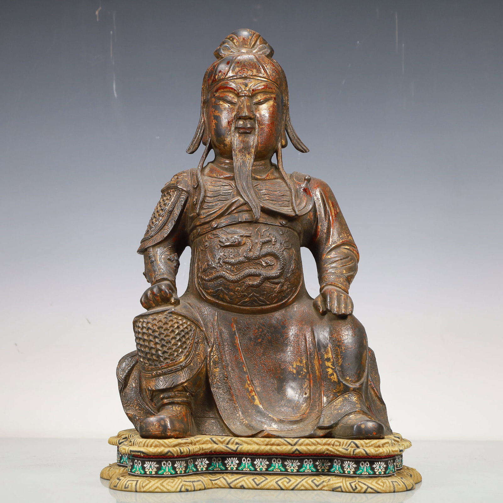 A Precious Gilt-Bronze Figure Of Guan Gong: A Precious Gilt-Bronze Figure Of Guan Gong. The bearded figure is seated with a meditative expression,body rendered clad in an armor,the belly area cast in detail with a sinuous,scaly dragon. Chinese