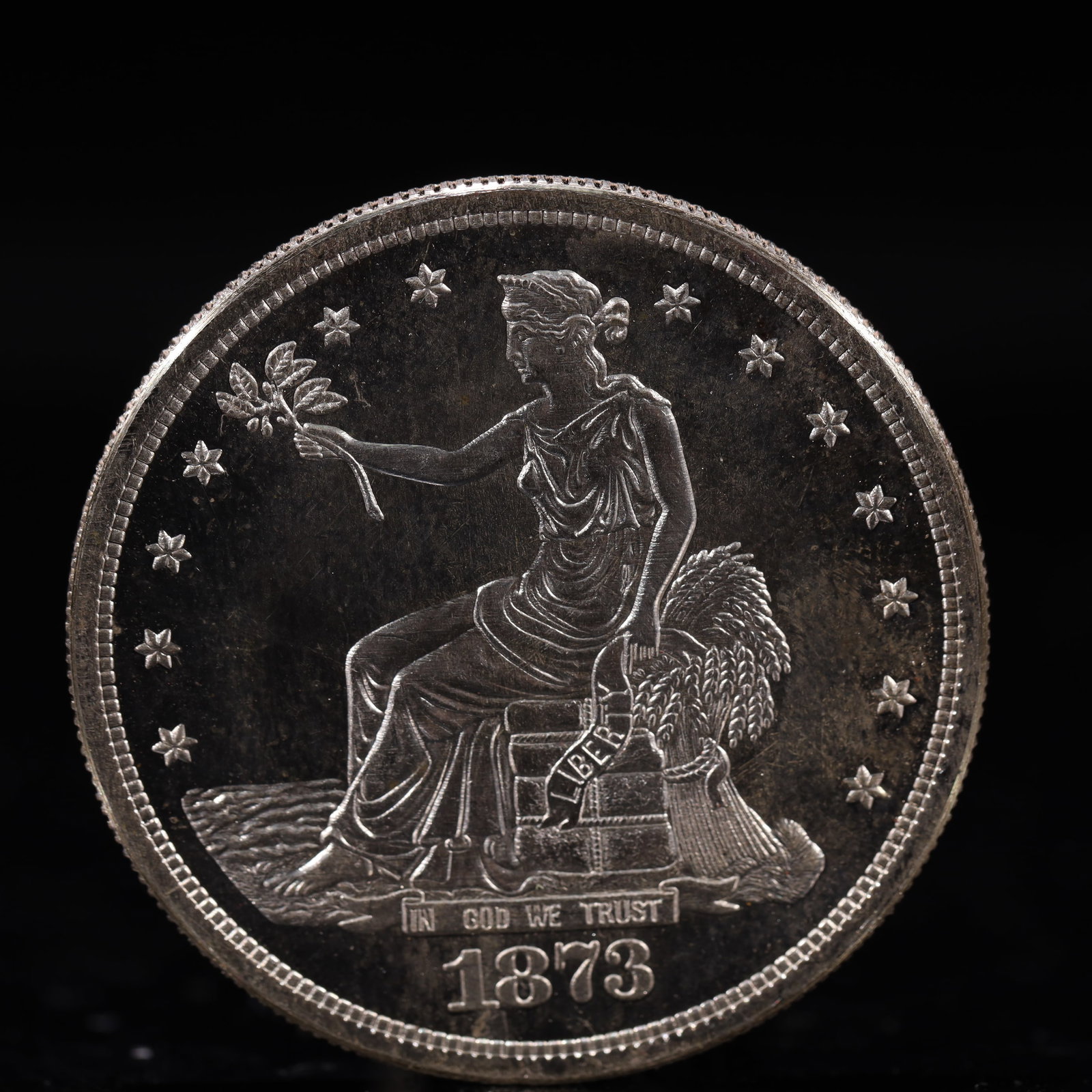 USA Trade Dollar 1873 Coin: American coin. Obverse: Liberty seated on a pedestal facing the sea to the left holding olive branches surrounded by 13 stars. IN GOD WE TRUST / LIBERTY / 1873. Reverse: An eagle holding branches with