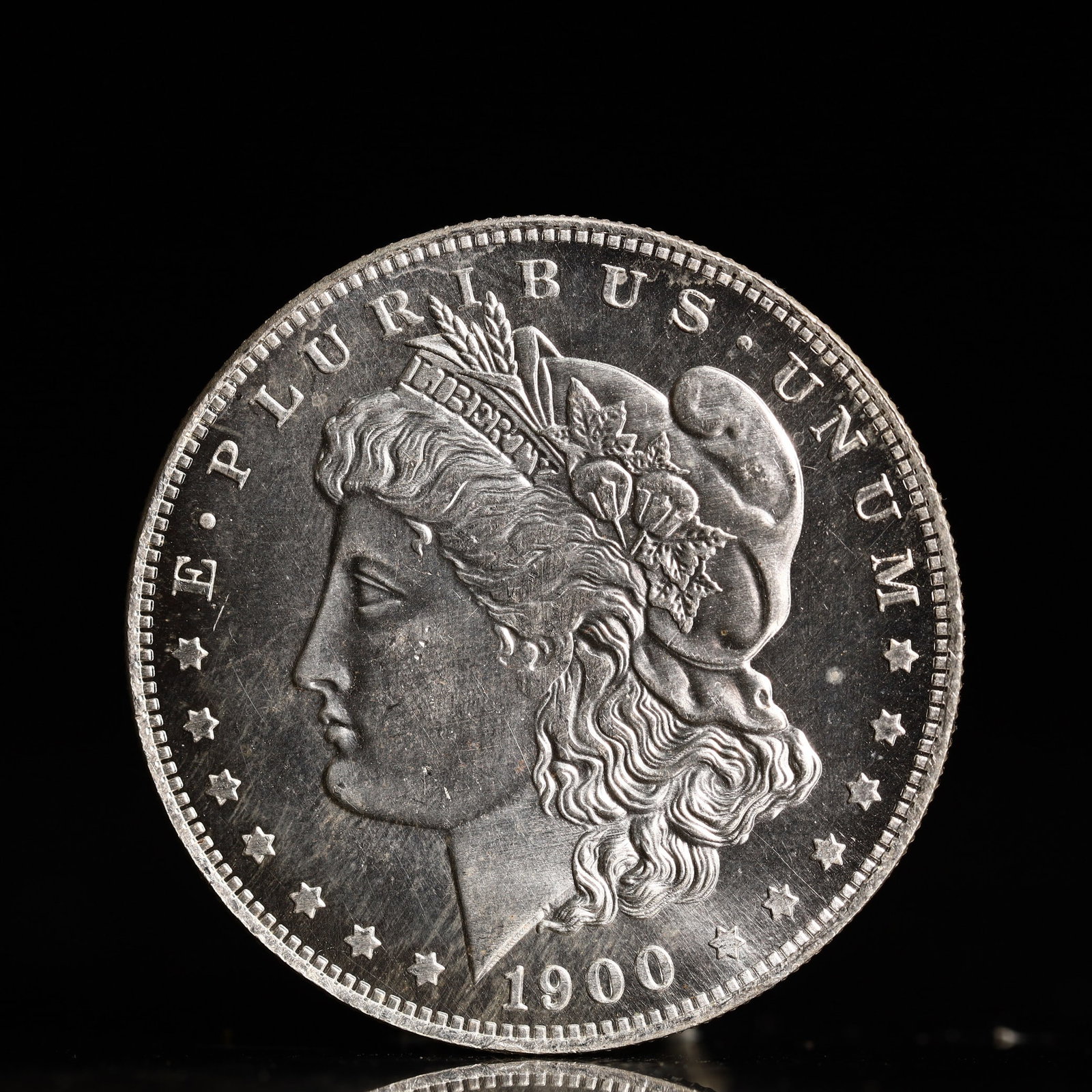 USA Morgan Dollar 1900 Coin: Obv: profile bust with date below and E PLURIBUS UNUM legend and stars around. Rev: eagle with In God we trust above within wreath with UNITED STATES OF AMERICA ONE DOLLAR legend. IN GOD WE TRUST / LI