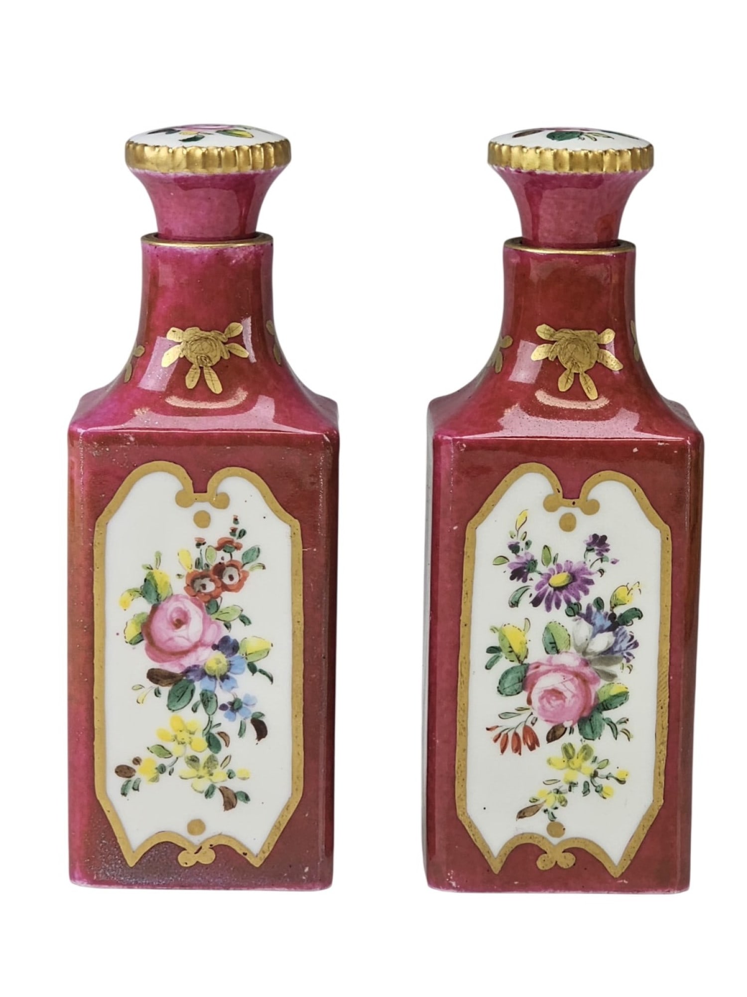 19TH CENTURY FRENCH SEVRES PORCELAIN PERFUME BOTTLES: This pair of 19th-century French porcelain perfume bottles is decorated in a deep rose Pompadour ground with hand-painted floral bouquets within gilded reserve panels. Each bottle features a square-se