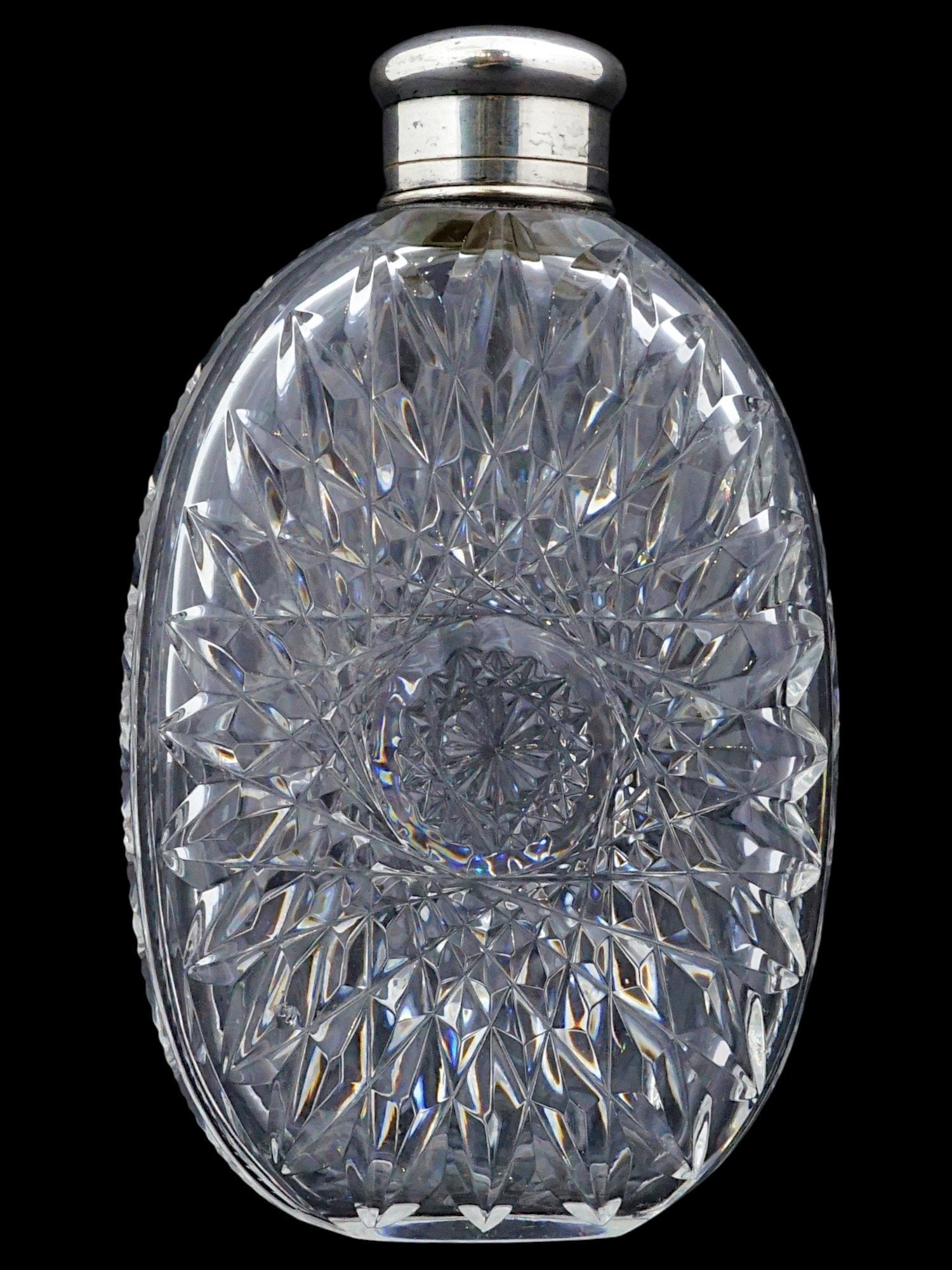 ANTIQUE CUT CRYSTAL FLASK WITH SILVER CAP: This antique pocket flask is crafted from heavy clear crystal featuring elaborate deep-cut geometric facets and a central starburst motif. The oval, flattened body is fitted with a polished silver scr