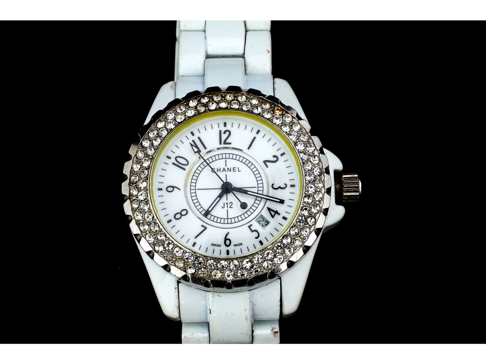 CHANEL J12 WHITE CERAMIC DIAMOND BEZEL QUARTZ WATCH: This Chanel J12 quartz wristwatch features a white ceramic case and a matching link bracelet equipped with a deployant clasp. The white dial displays black Arabic numeral hour markers, inner track mar