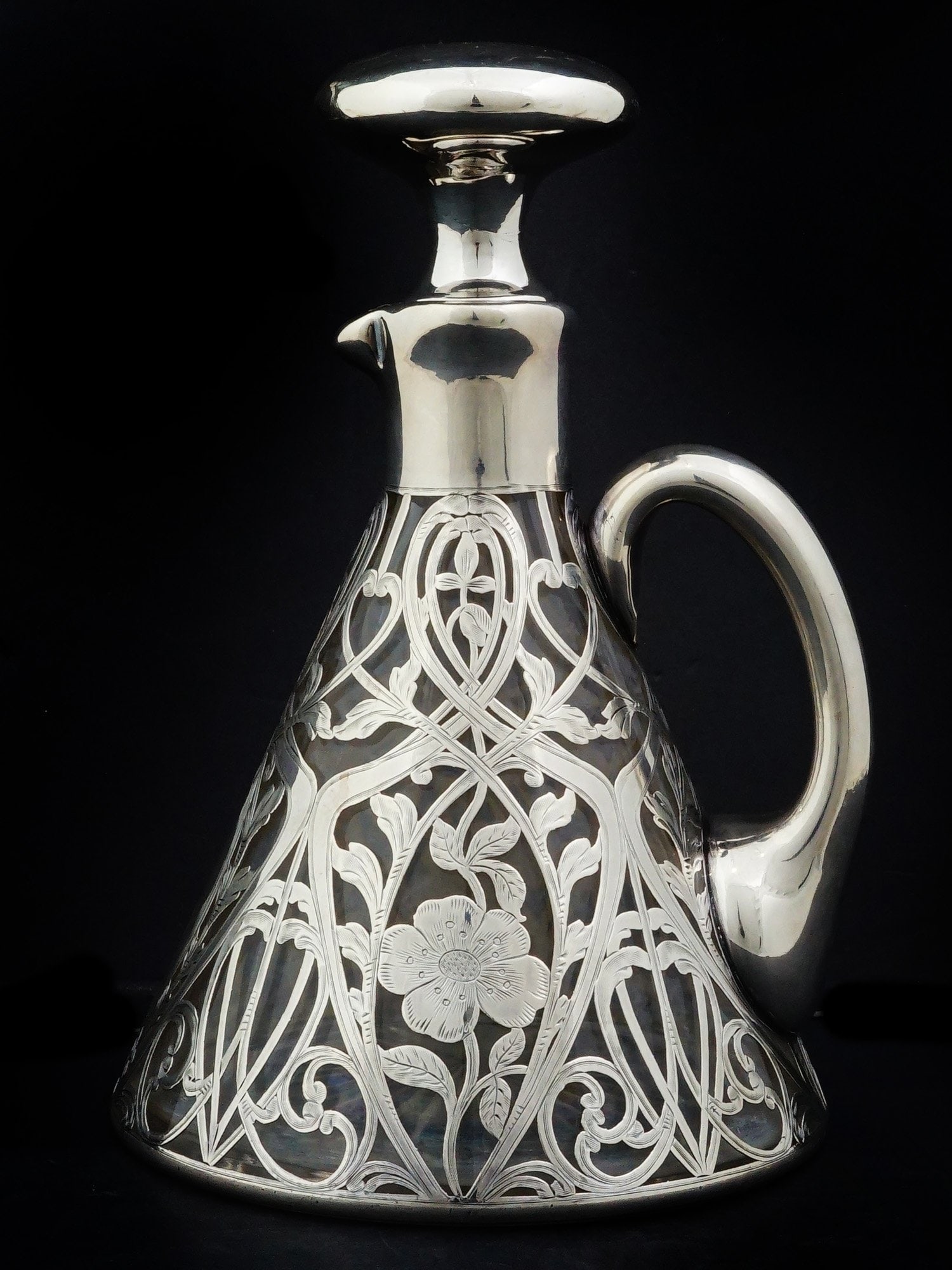 BLACK STARR AND FROST FINE SILVER AND CRYSTAL DECANTER: An antique American silver overlay and lead glass decanter by Black, Starr and Frost. Dated early 20th century. The cone body is enclosed in pierced Art Nouveau floral ornaments with etched detailing.