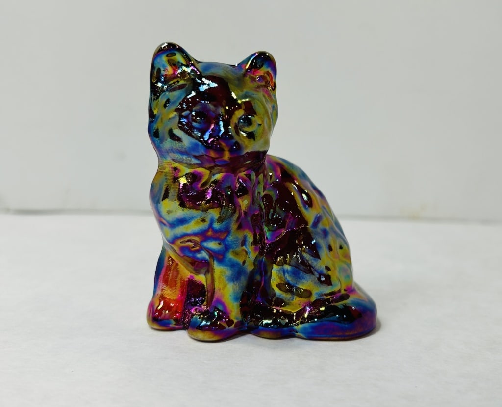 Mosser Iridescent Carnival Glass Sitting Cat: The piece is made of pressed glass with a heavy iridescent carnival coating that displays a multicolored metallic luster including shades of purple, blue, gold, and red. The cat is modeled in an uprig