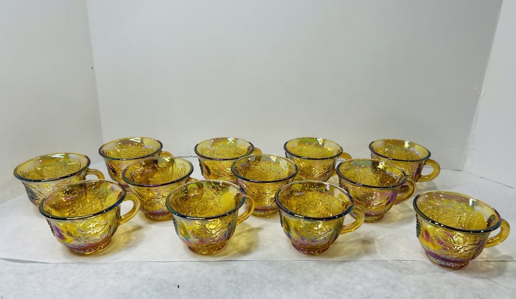 Set of 12 Marigold Carnival Glass Punch Cups: This set of 12 marigold carnival glass punch cups is attributed to the Indiana Glass Company and features the Harvest Grape pattern. The cups are made of pressed glass with a metallic iridescent finis