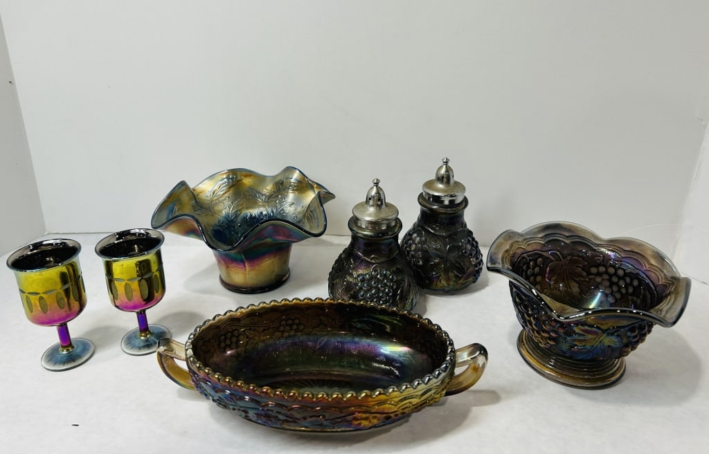 A Collection of Northwood and Other Iridescent Carnival Glass Tableware: An assortment of iridescent carnival glass tableware in various forms and finishes, primarily featuring relief-molded grape and leaf motifs. The collection includes pieces in a deep amethyst hue, such